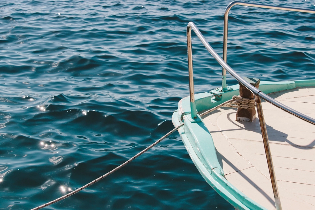 Bow of a moored boat with mooring line on sparkling water