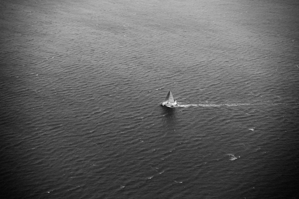 Lone sailboat under way on open water, seen from above